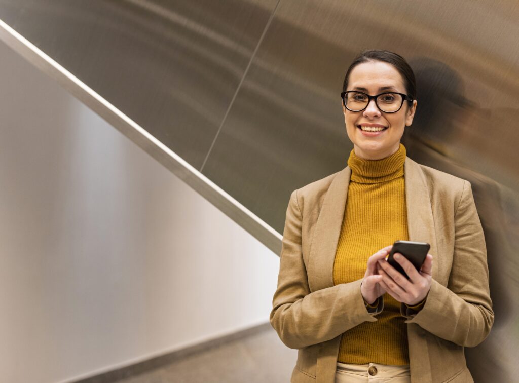 Mujer de negocios sonriendo con un celular en mano, representando la transformación digital del mercado financiero