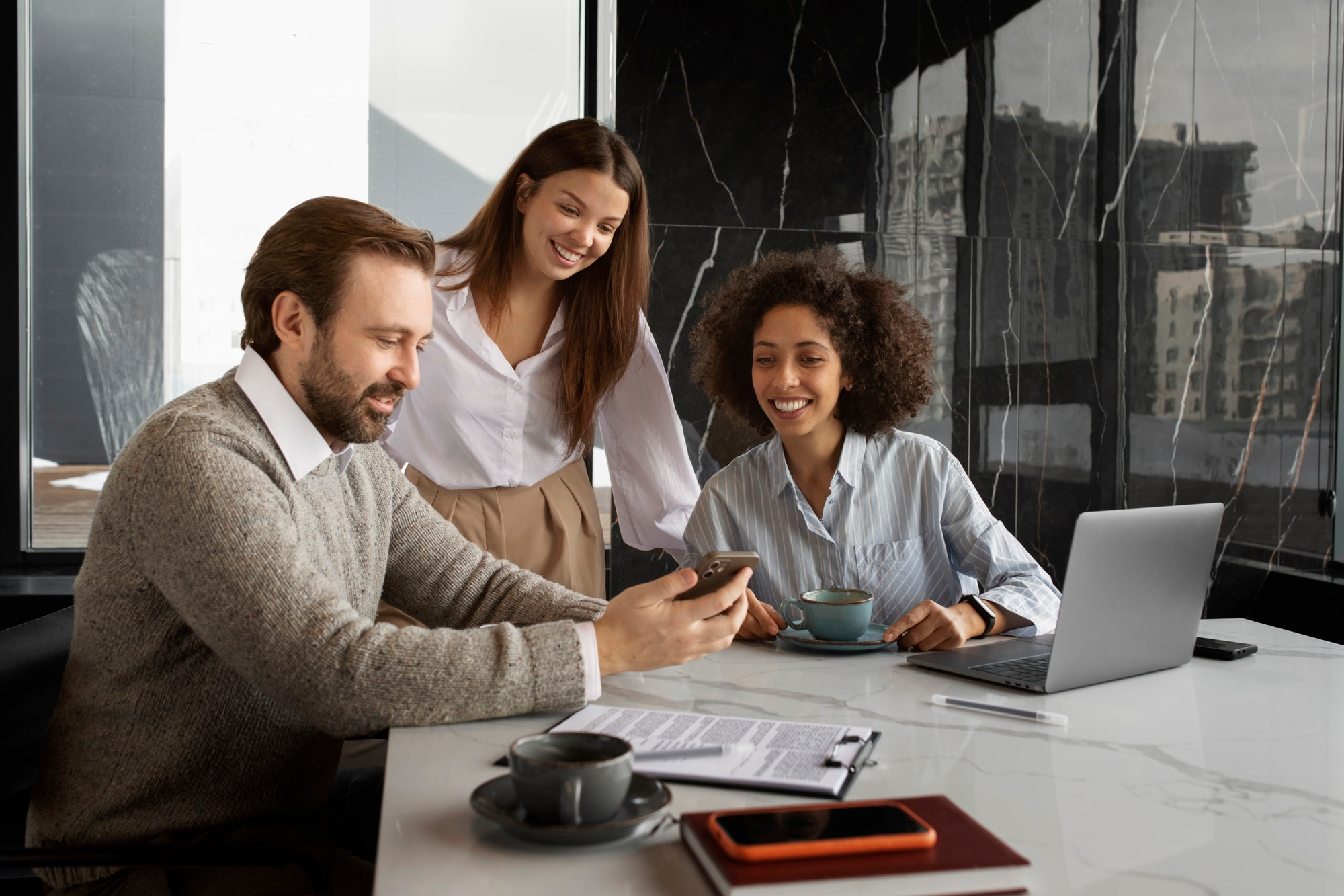 Três pessoas em ambiente corporativo, reunidas ao redor de uma mesa com notebook e documentos, representando colaboração e tecnologia aplicada à segurança de dados.